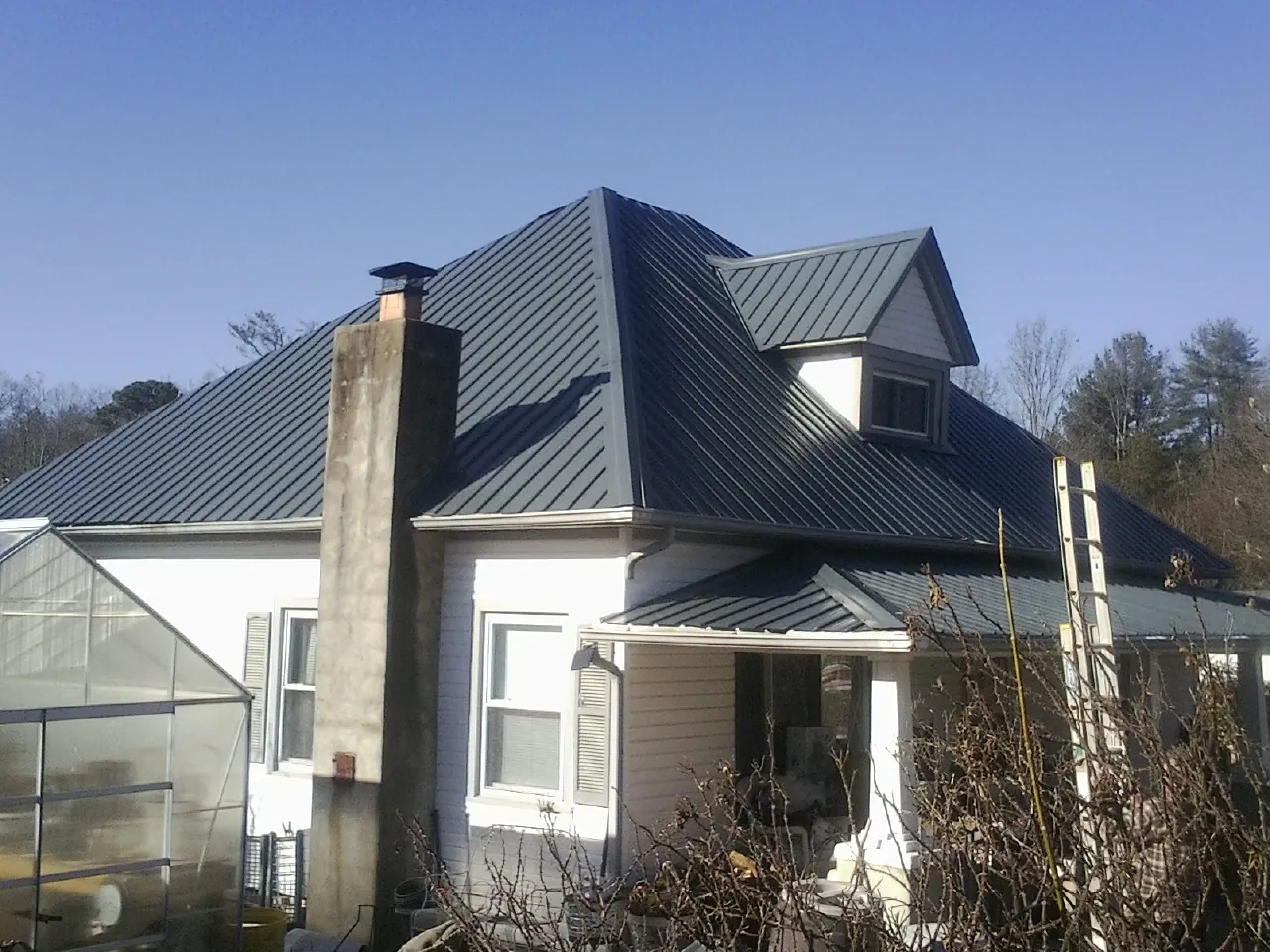 Dark blue standing seam metal roof on a white farmhouse with dormer — Slate & Tile Roof Repair by Roofing Brothers in Sumiton