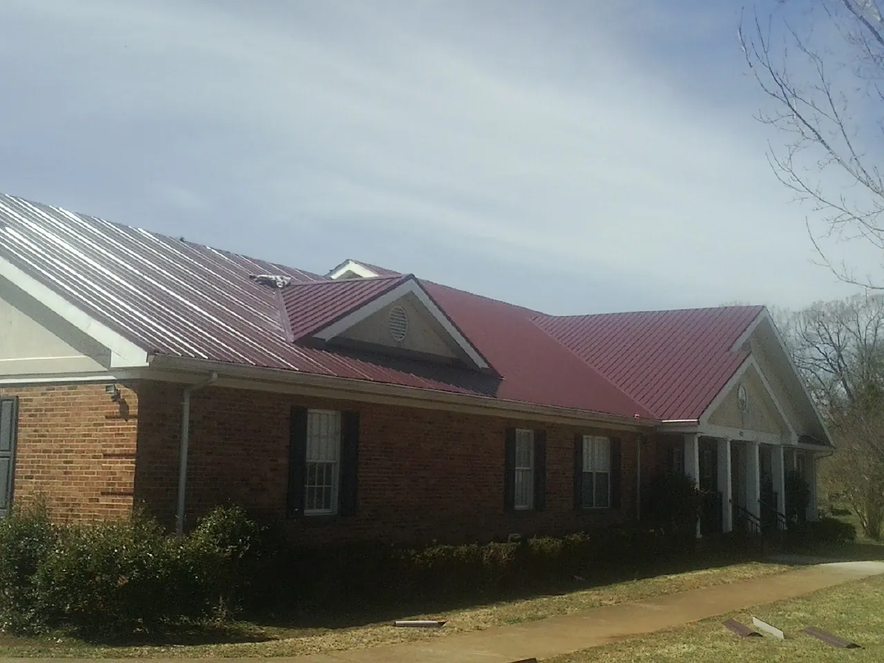 Red metal roof with gabled entries on a long brick building, from a Hail Damage Roof Repair job in Sumiton