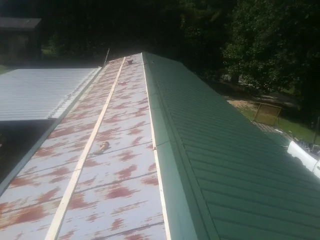 Old rusted panels beside newly installed green metal roofing — Wind Damage Roof Repair by Roofing Brothers in Sumiton