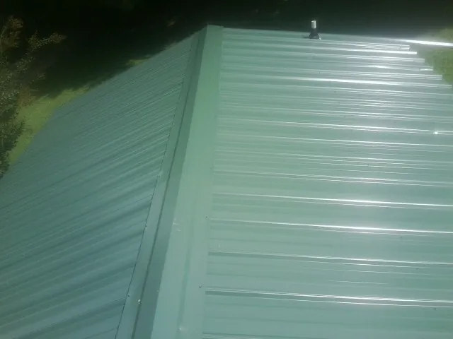 New green metal panels meeting at the ridge of a roof — Flat Roof Repair work by our crew in Sumiton