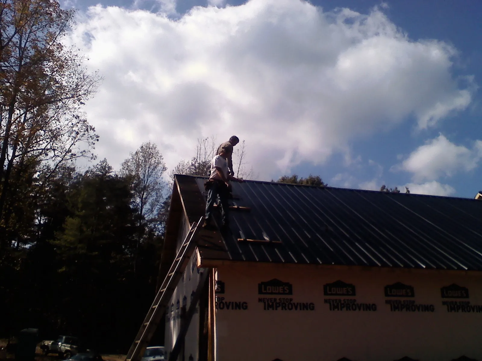 Roofer fastening dark metal panels high against a cloudy sky, from a Roof Inspection job in Sumiton