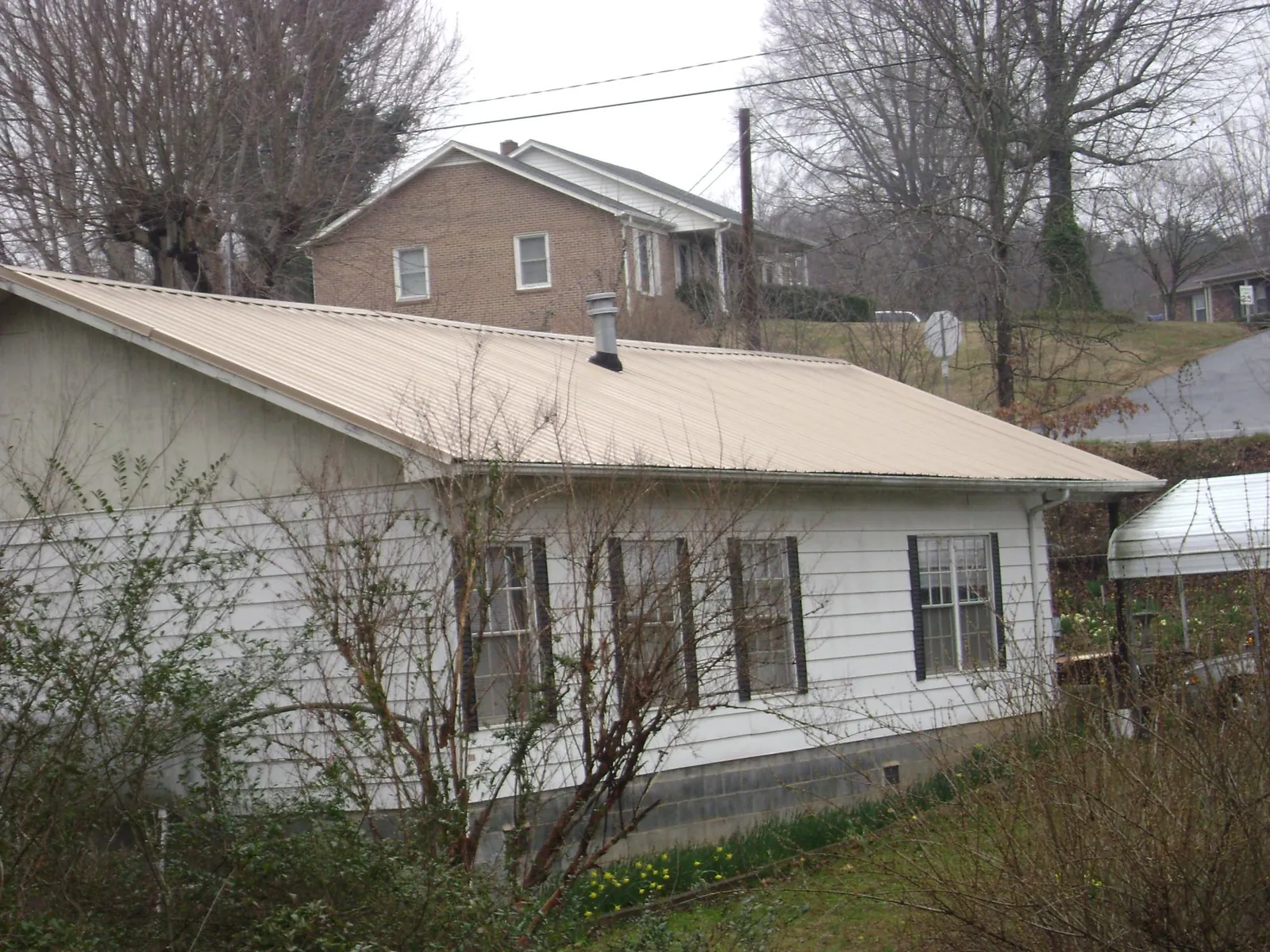 Tan metal roof on a white sided house set into a hillside — Commercial Roofing by Roofing Brothers in Sumiton