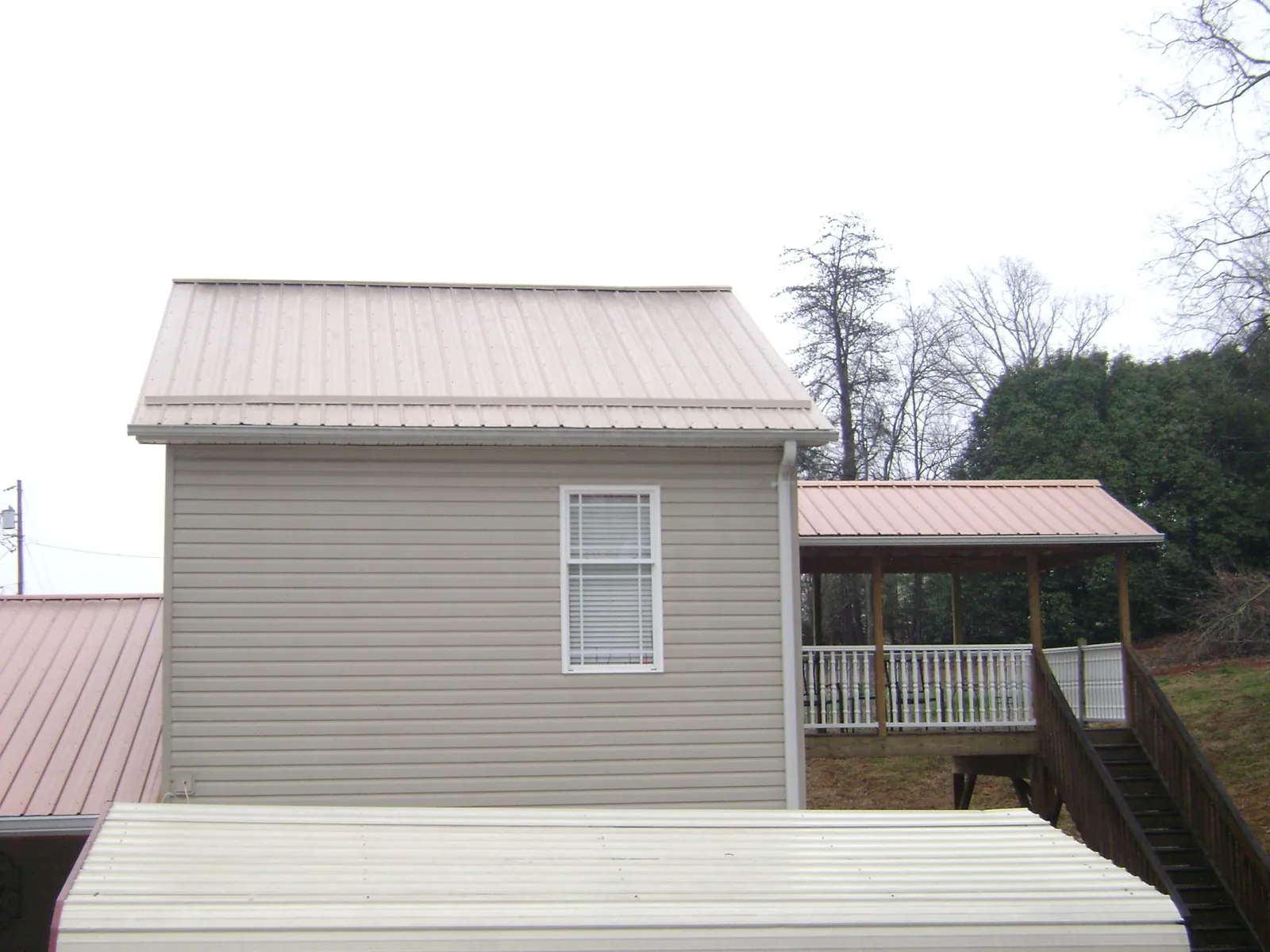 Tan metal roofs on a two story addition and attached porch, from a Roof Replacement job in Sumiton